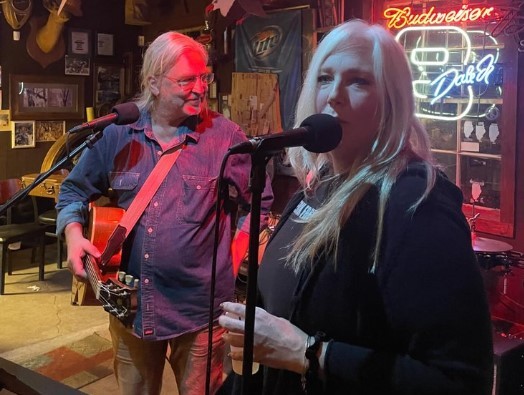 a man and a woman sing and play guitars on a stage